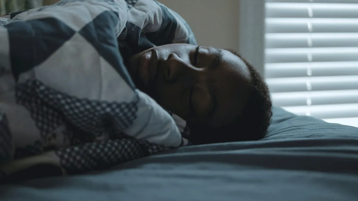 A man asleep under a patterned quilt in soft morning light